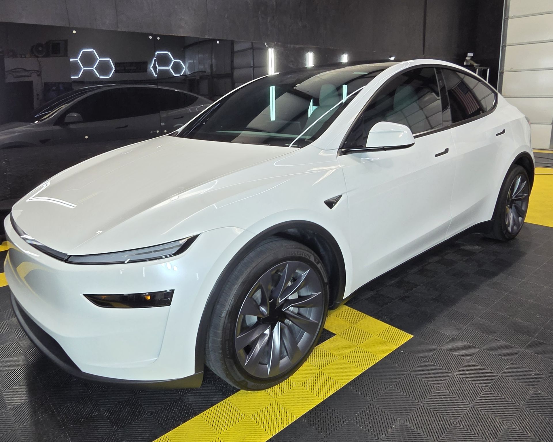 White Tesla SUV parked indoors on a yellow line in a showroom or garage