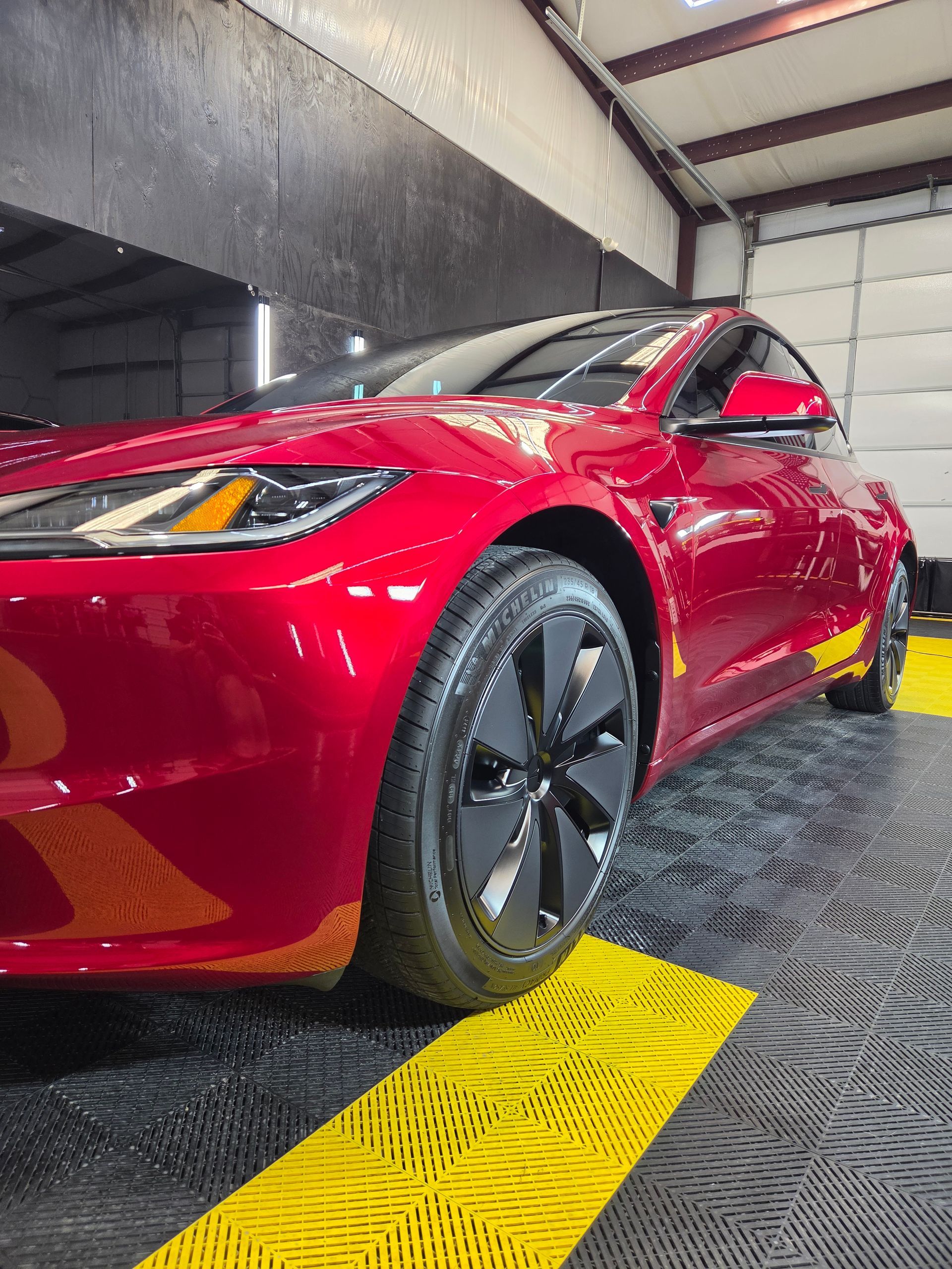 Red car parked indoors on a yellow textured floor ramp, front-left view.