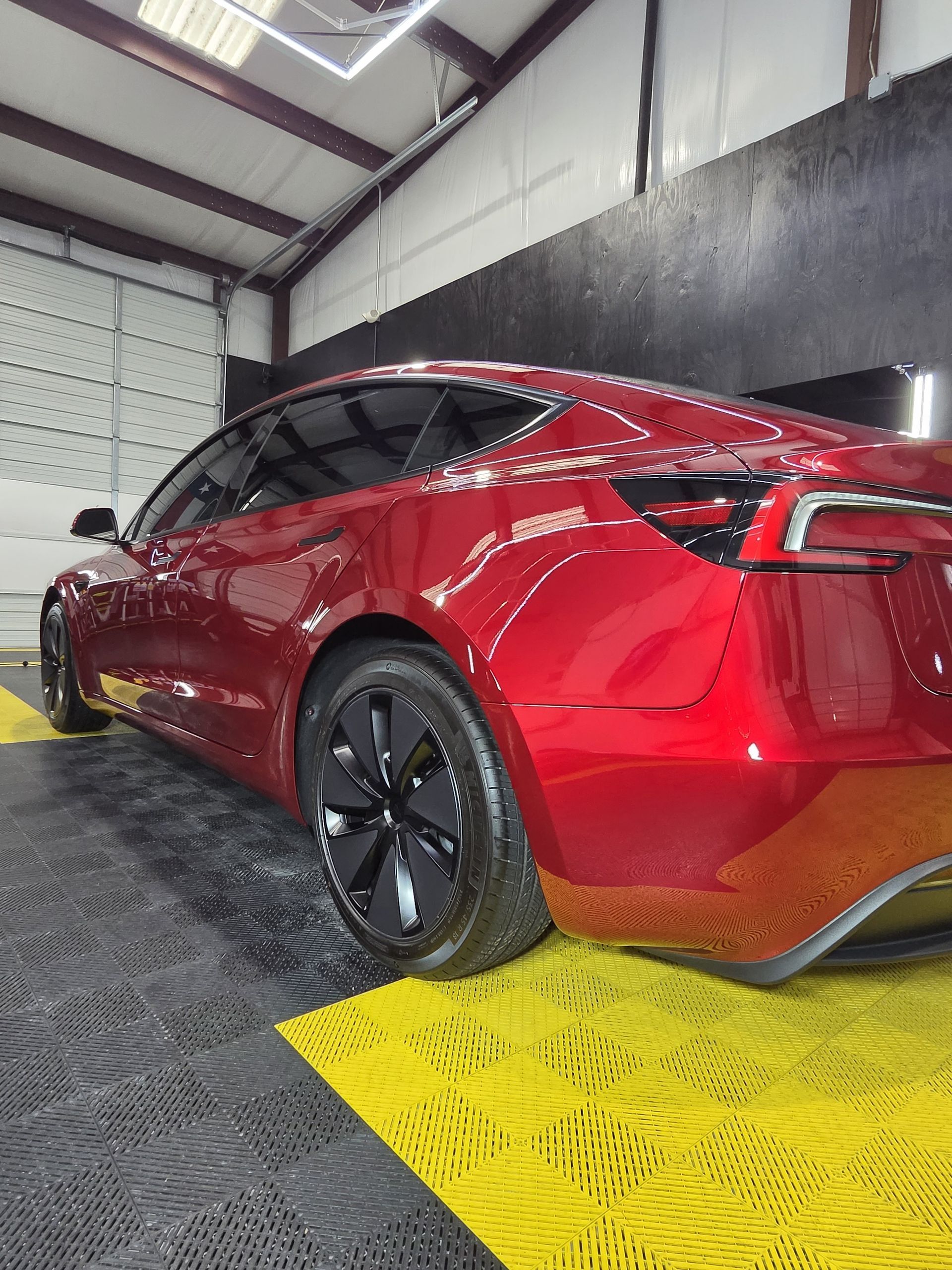 Red sports sedan in a car wash bay, wet and glossy, with black wheels and yellow floor mat.