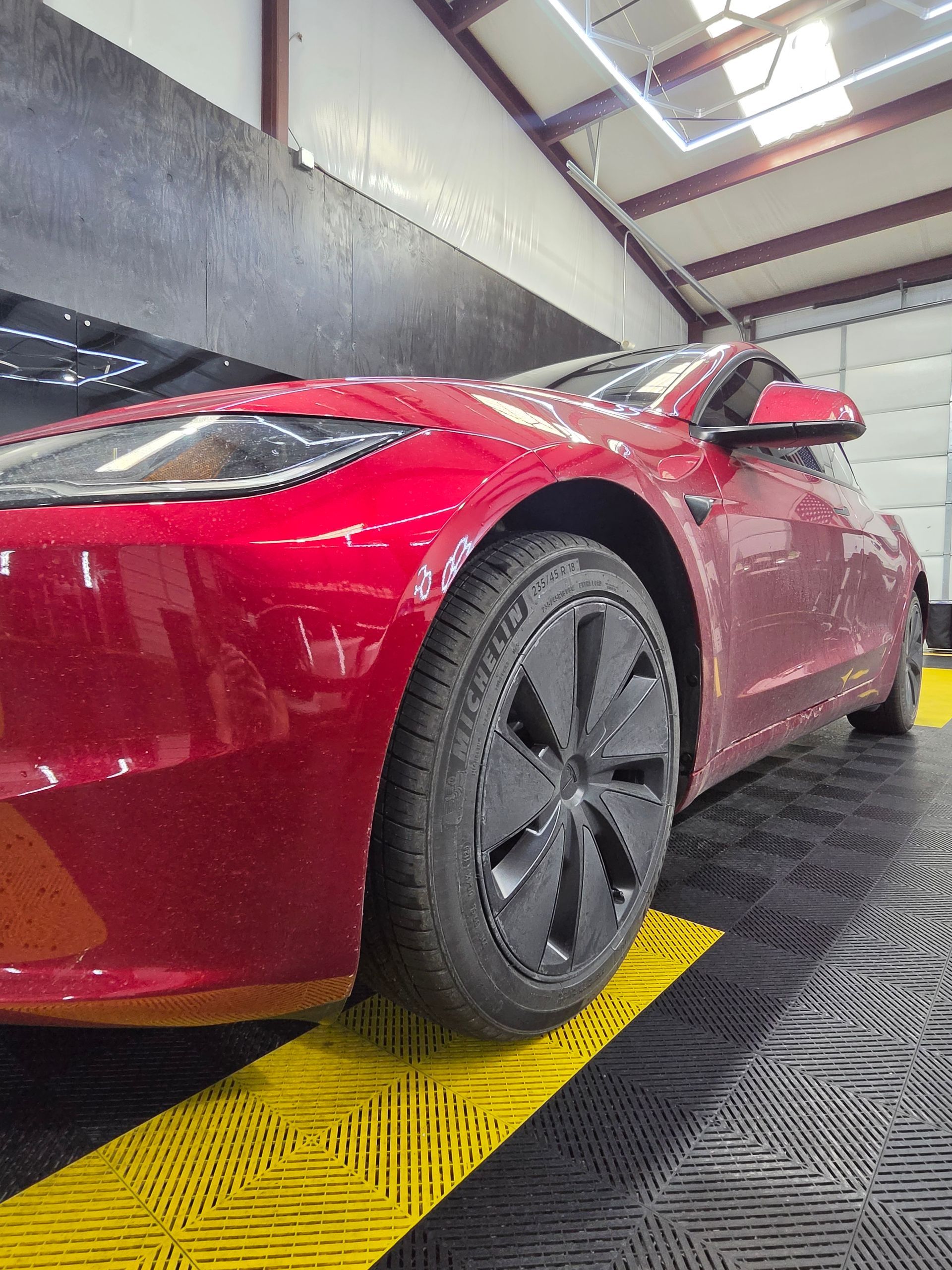 Red sports car in a parking garage, viewed from the front side on a yellow floor ramp.