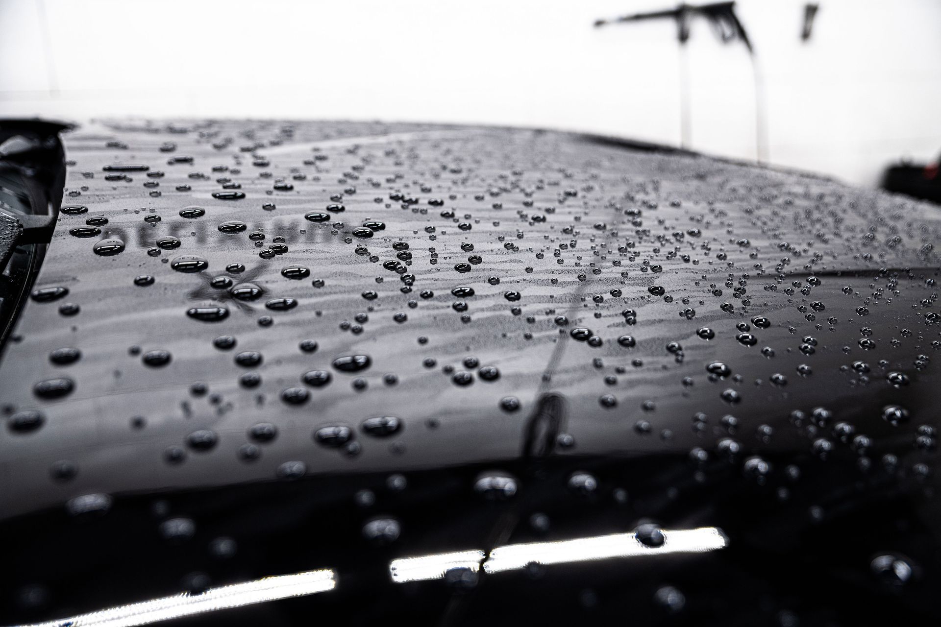 Rain droplets on a black car hood in a garage