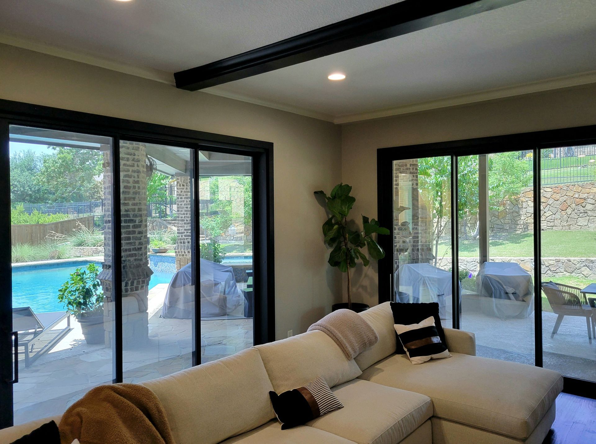 Living room with pool view, beige sofa, black trim windows, and an indoor plant.