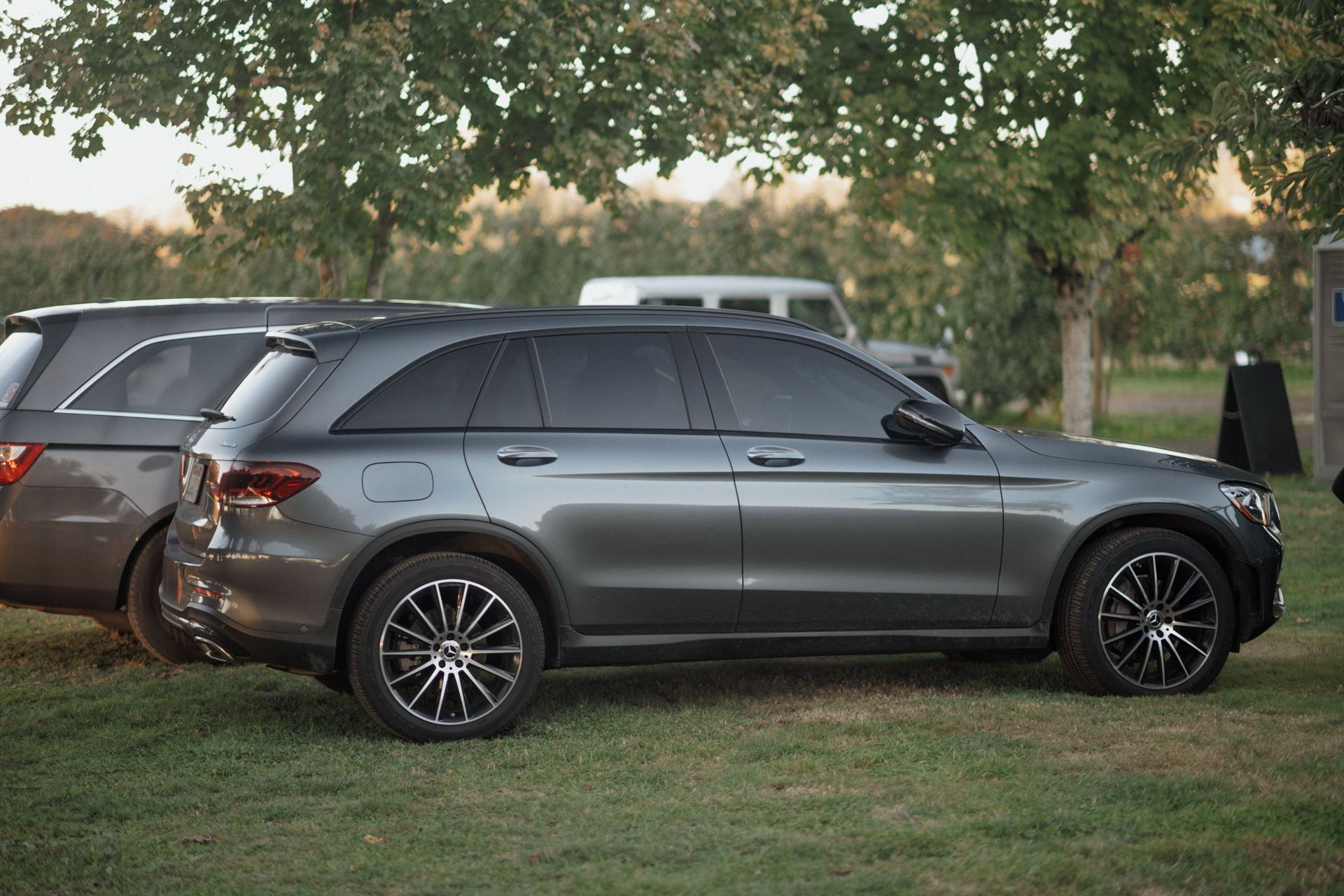 Dark gray SUV parked on grass under trees beside another vehicle at dusk