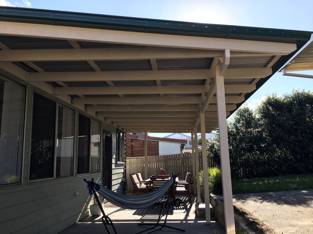 A Hammock Is Sitting Under A Covered Porch Next To A House — Newcastle Patio Covers In Port Stephens, NSW