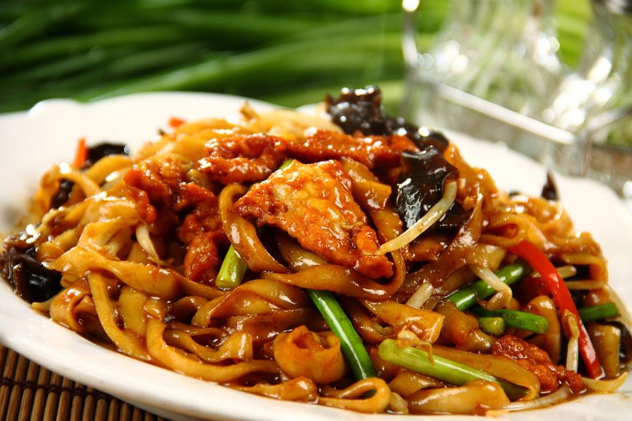 Primo piano di spaghetti saltati in padella con pollo, verdure e cipollotti, serviti su un piatto bianco.