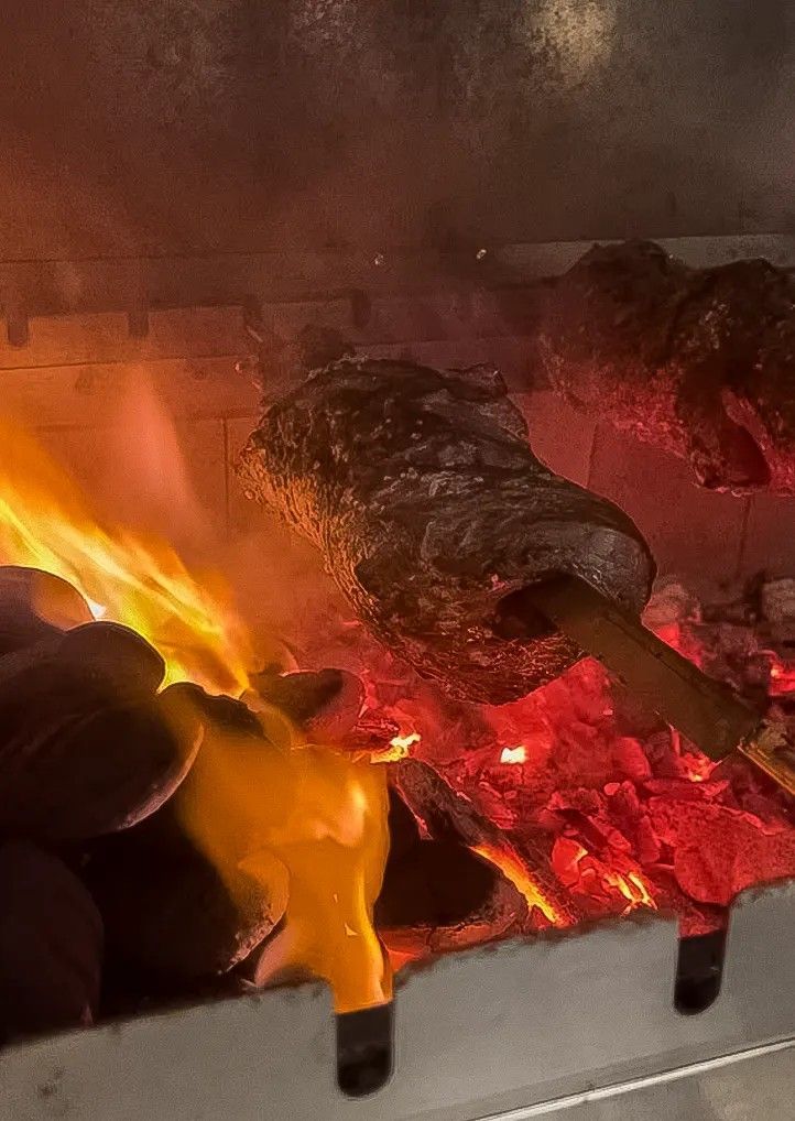 Legna che brucia e braci ardenti in un camino, con fiamme arancioni brillanti e fumo.