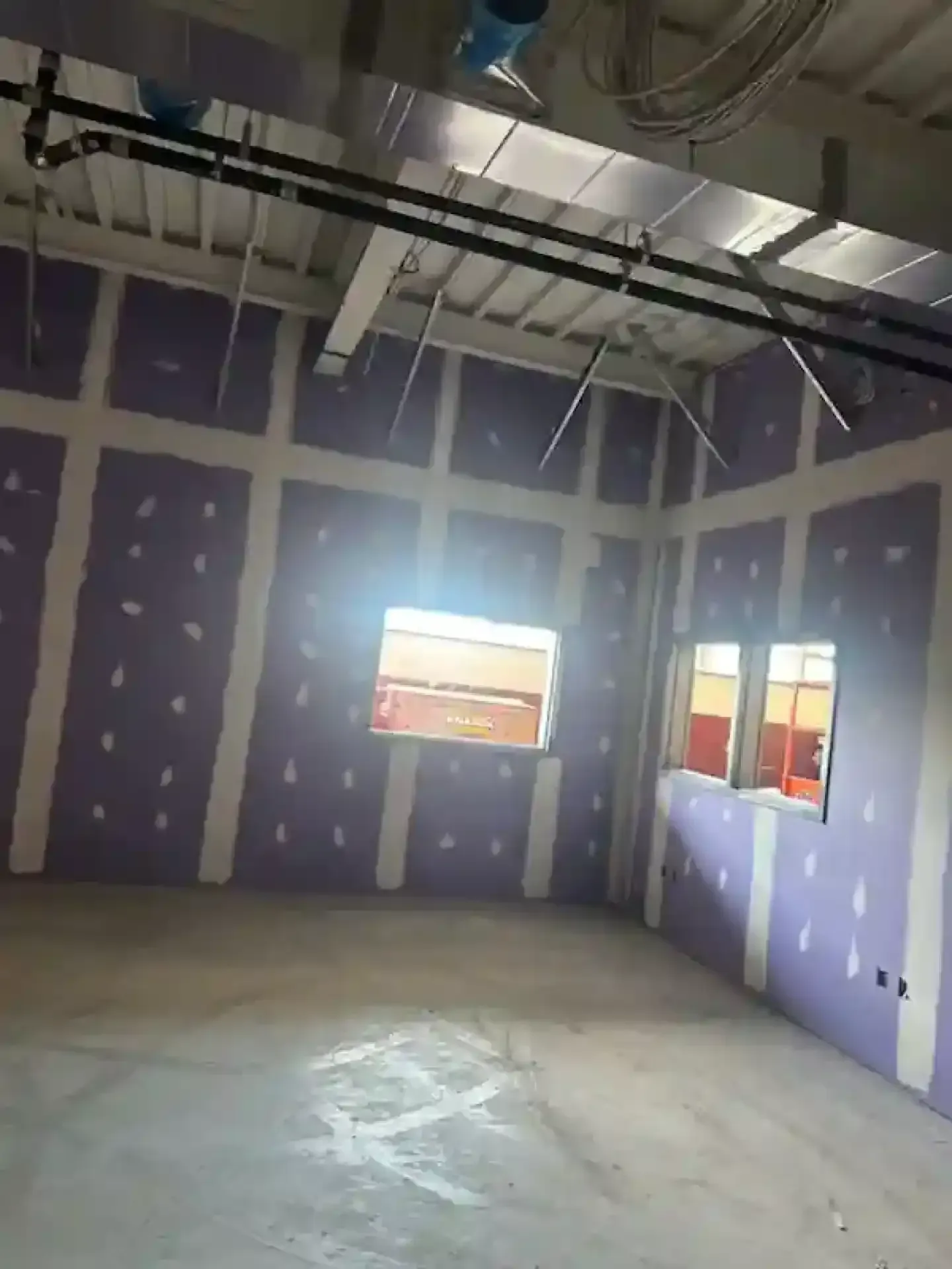 Empty unfinished room with purple drywall, exposed ceiling beams, and two windows.