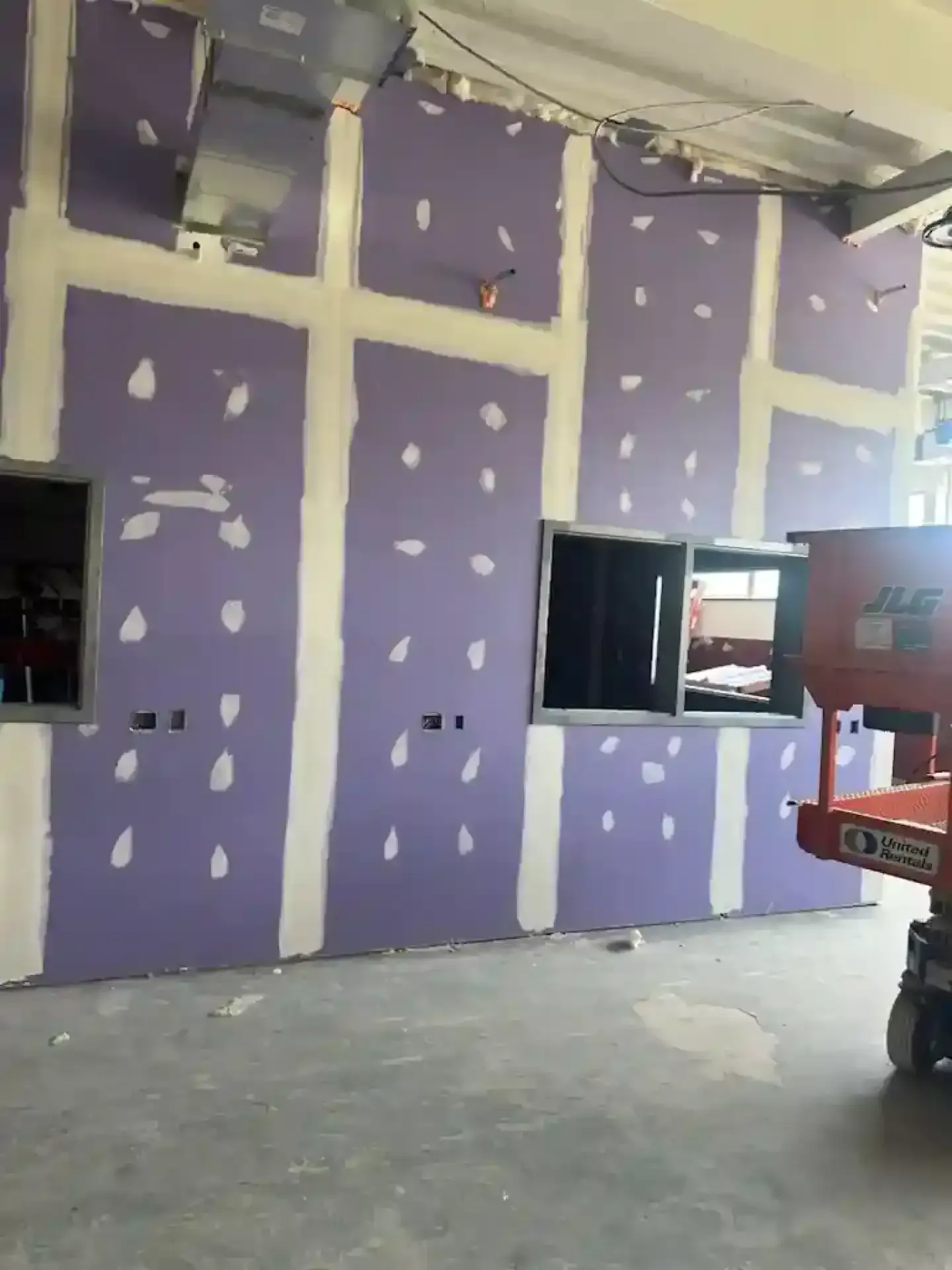 Purple drywall in an unfinished room with white patching and exposed ceiling, next to a window opening.