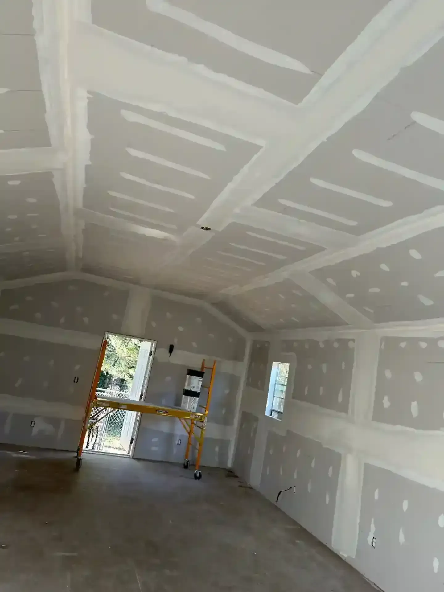 Unfinished drywall room with taped seams, a window, and a door opening to daylight.
