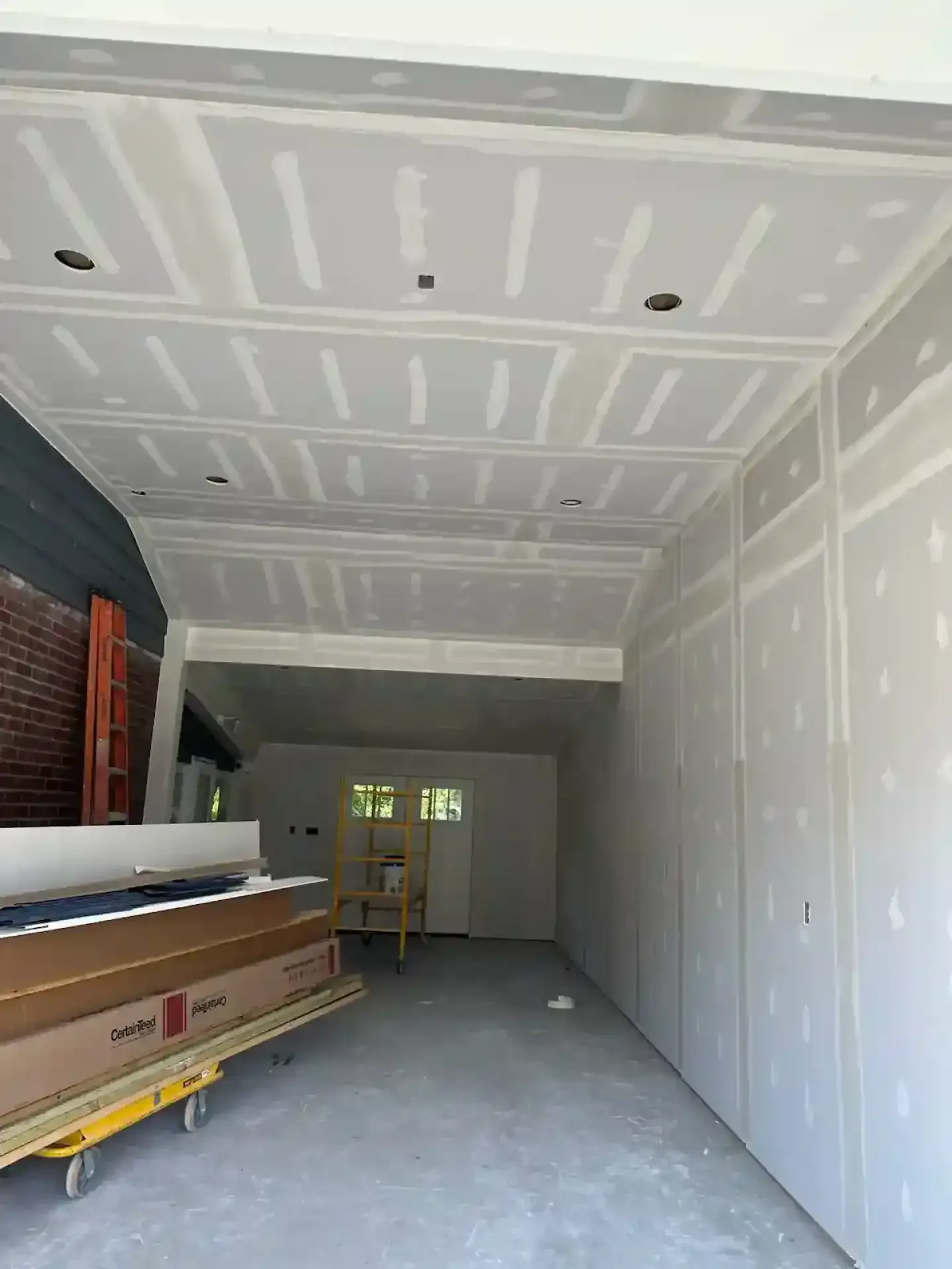 Unfinished interior with drywall, long narrow room, stacked materials, and a doorway at the far end.