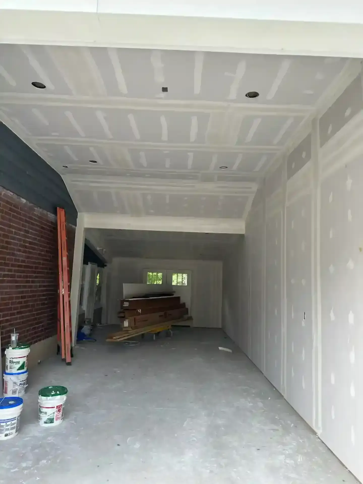 Unfinished garage interior with drywall, concrete floor, brick side wall, and stacked materials at the back