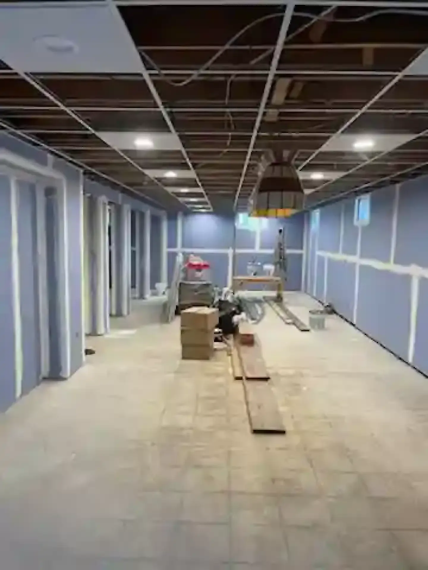 Empty indoor room under construction with exposed ceiling and blue wall panels, tools on the floor.