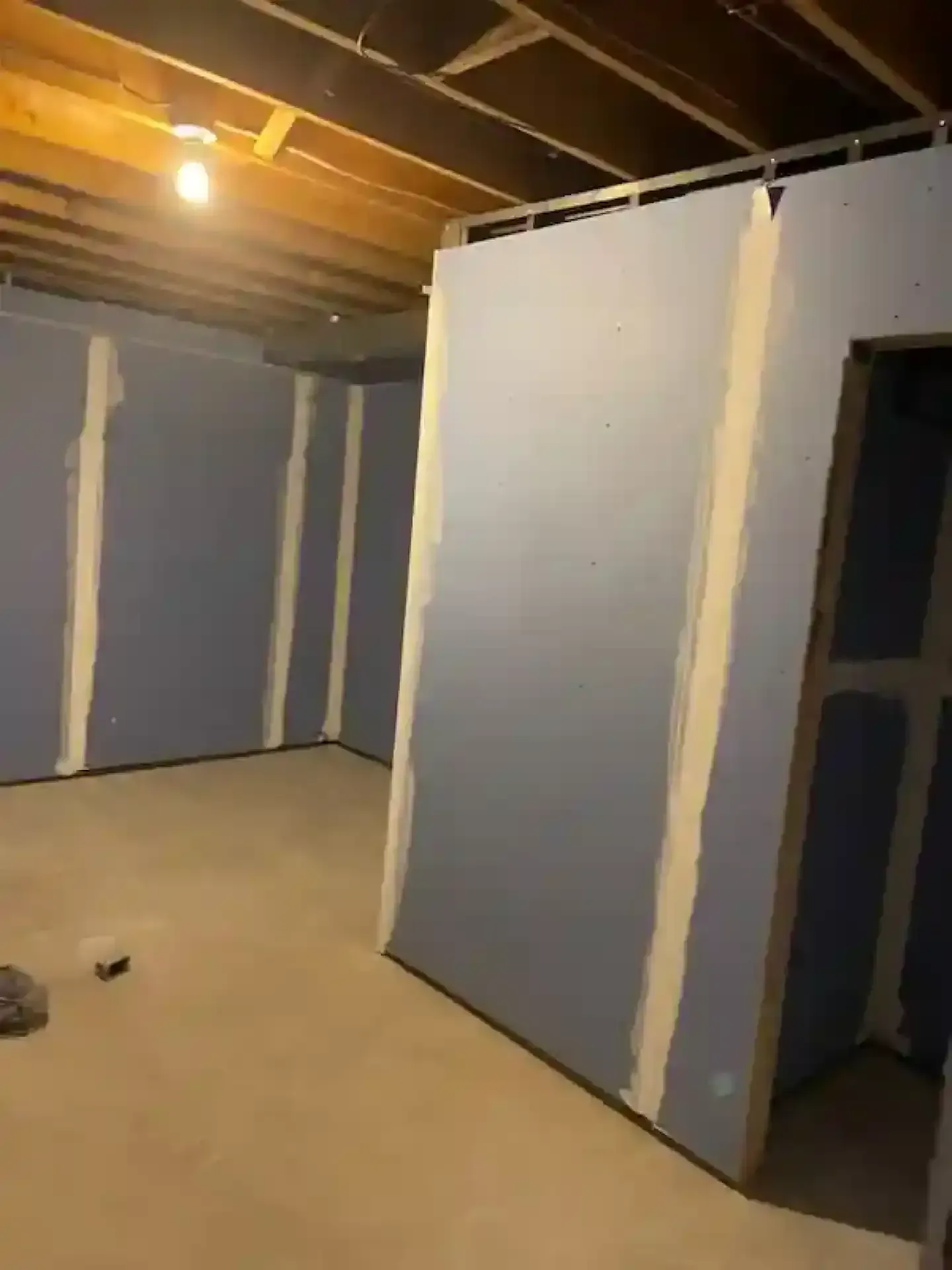 Unfinished basement room with blue-gray drywall, exposed ceiling joists, and a single bare bulb.