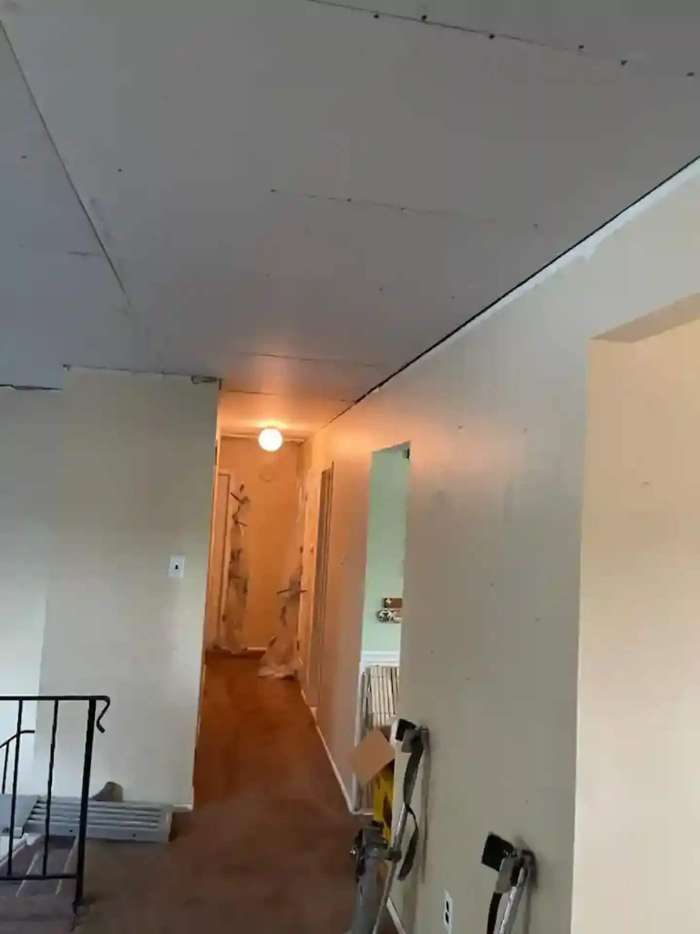 Narrow hallway with white walls, warm light, and a partially open doorway leading to a cluttered room
