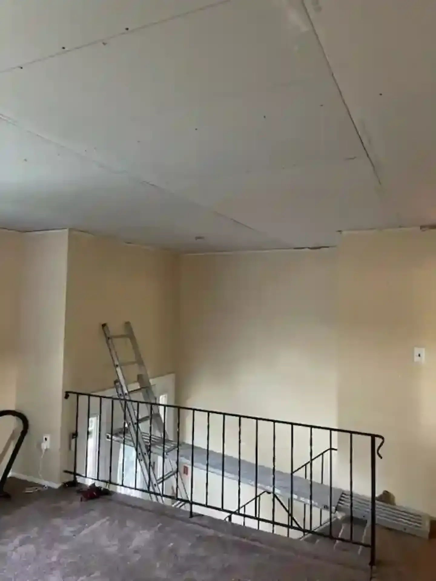 Empty beige room with a low railing, ladder, and exposed ceiling panels