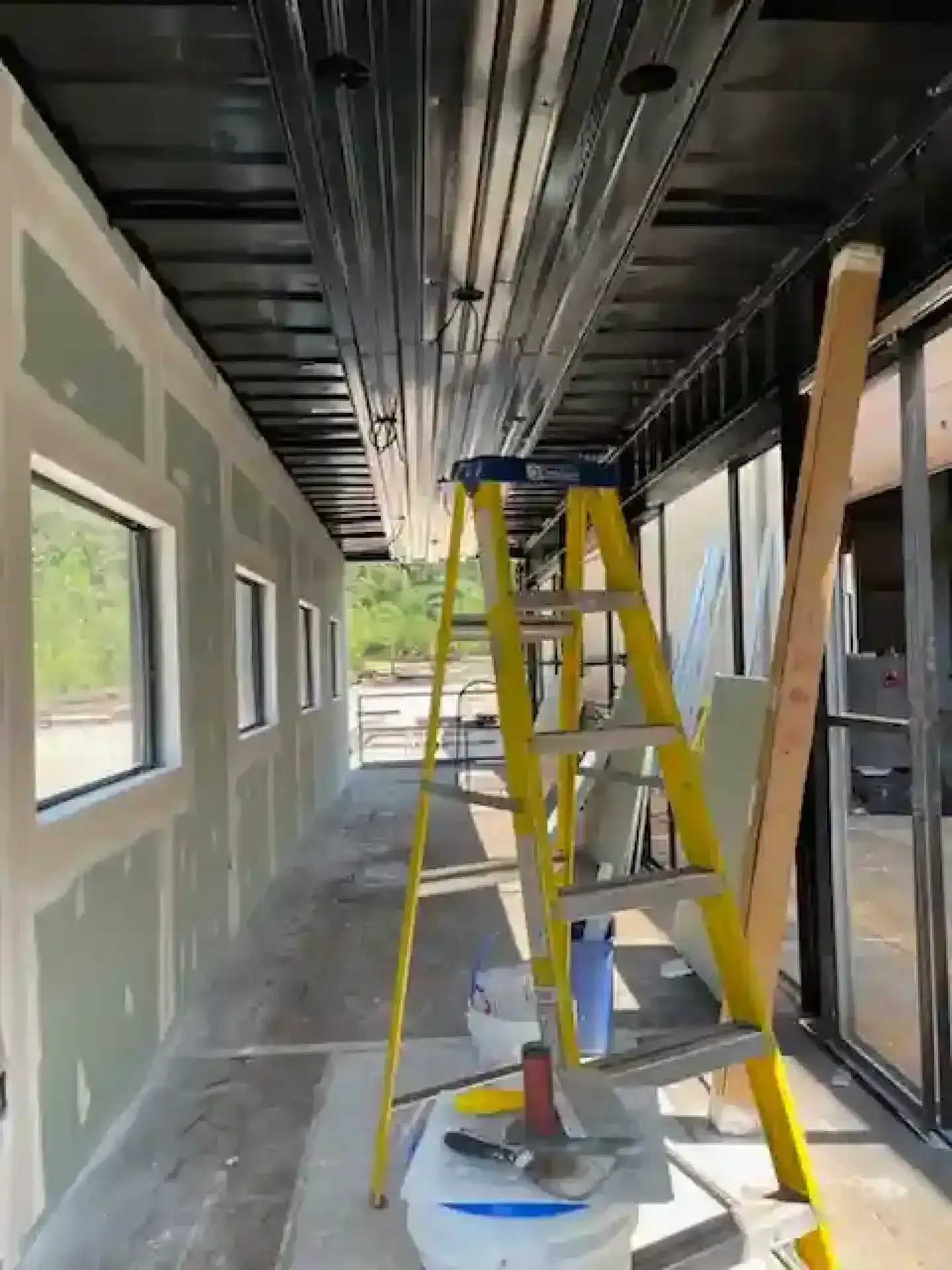 Yellow ladders in a narrow interior hallway under construction, with unfinished walls and ceiling.