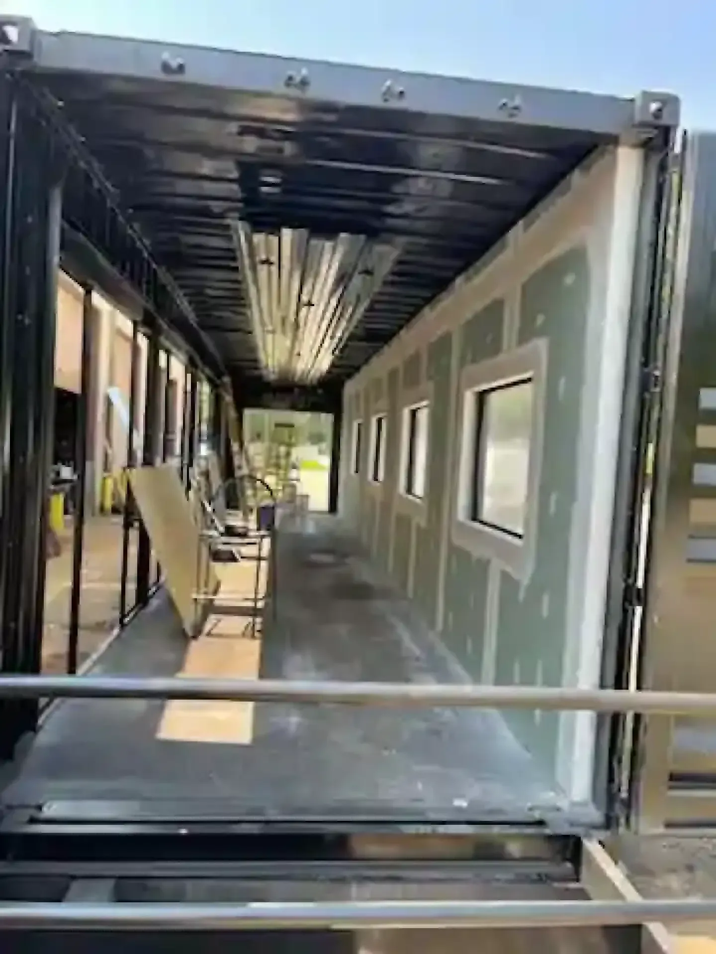 Interior of a partially built modular room with windows, metal framing, and a walkway inside a container-like structure
