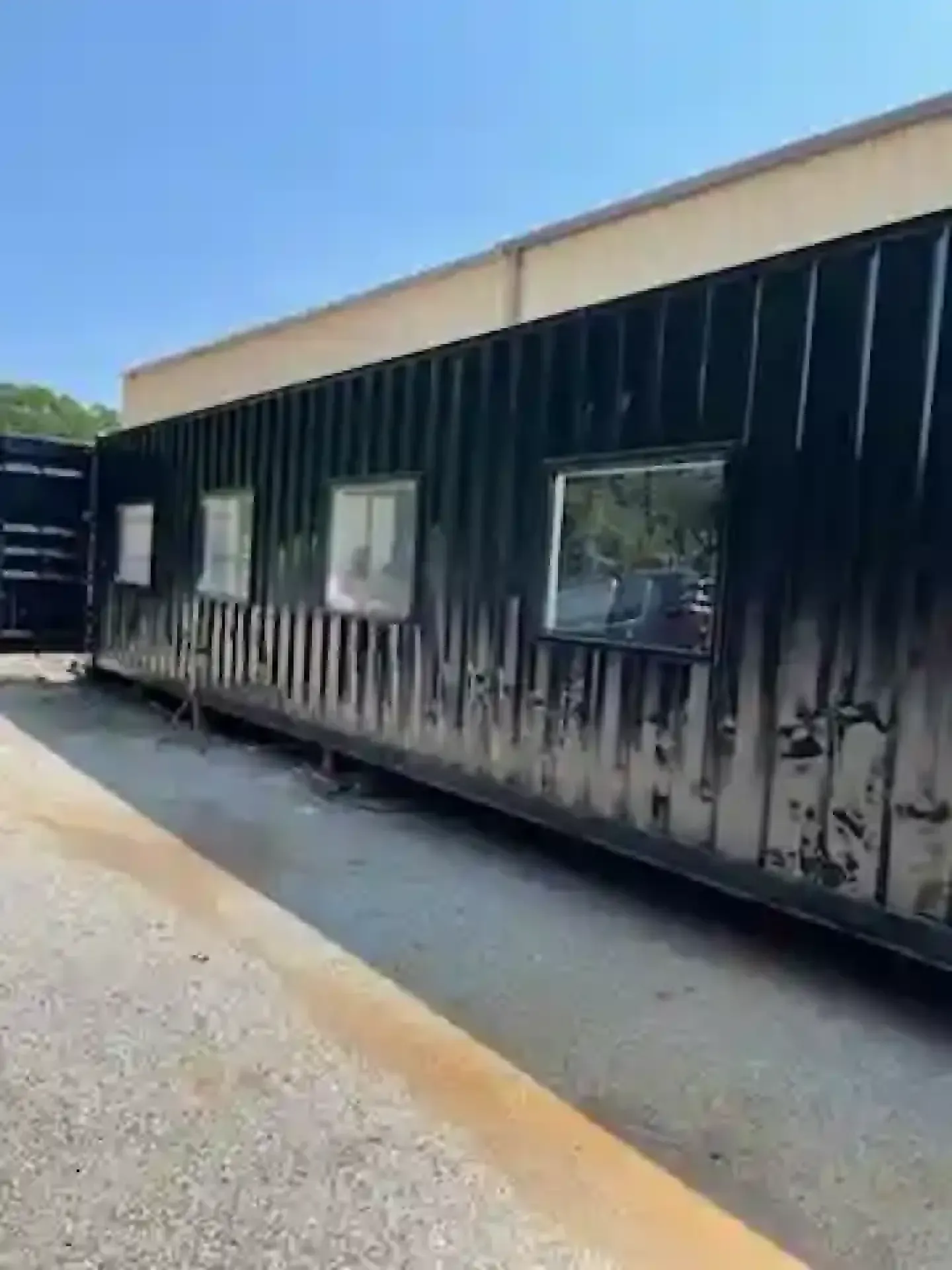 Soot-stained building exterior with windows and charred siding along a paved area under a blue sky