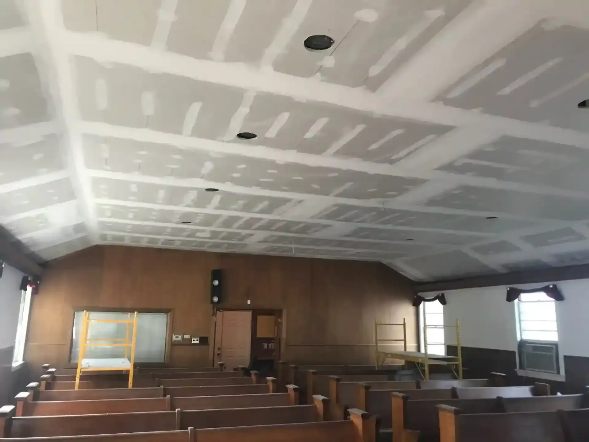 Empty unfinished room with drywall ceiling, wood-paneled walls, and rows of seats or benches.