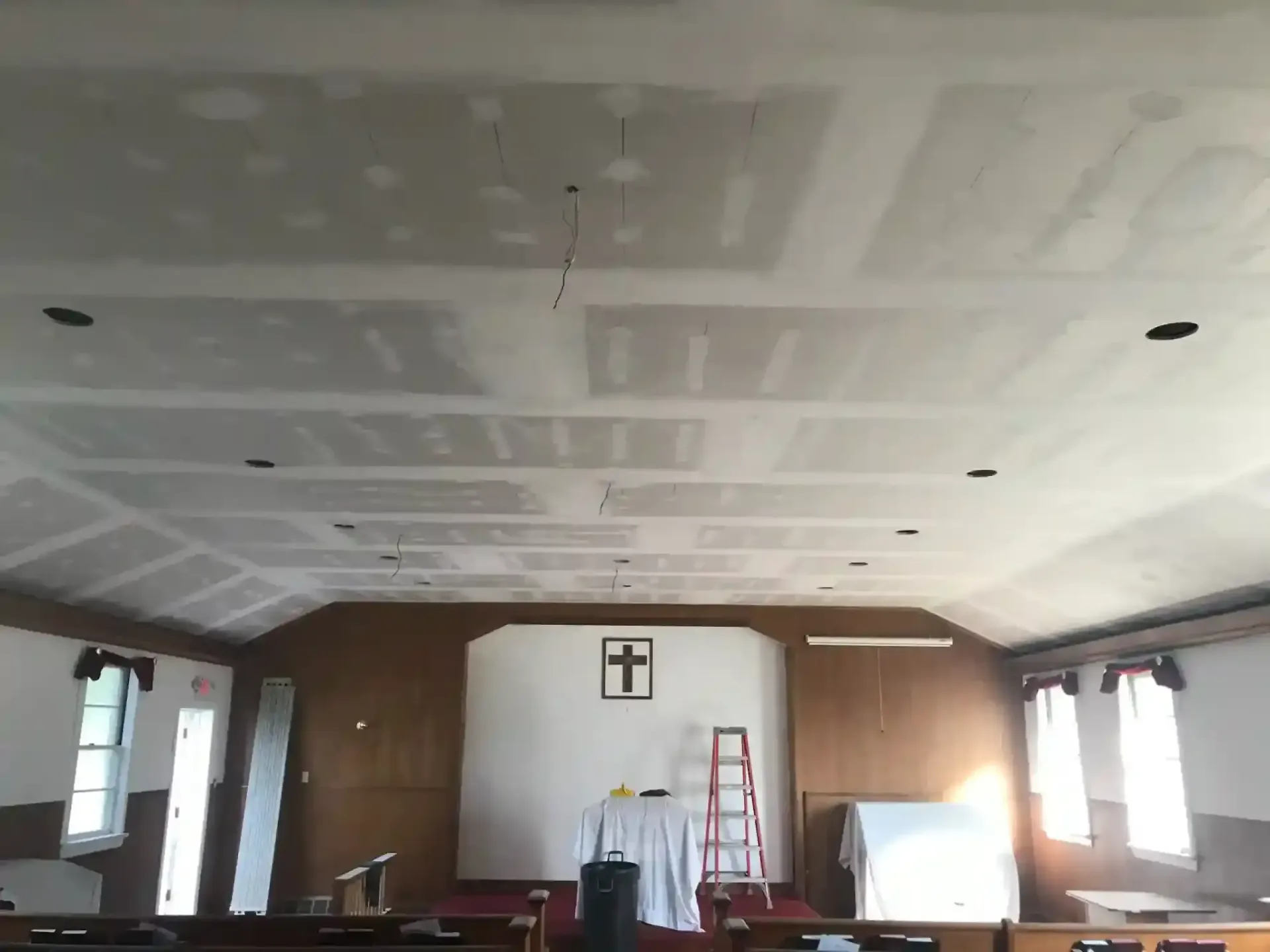 Empty room with unfinished drywall ceiling, windows, and a red ladder near the back wall.