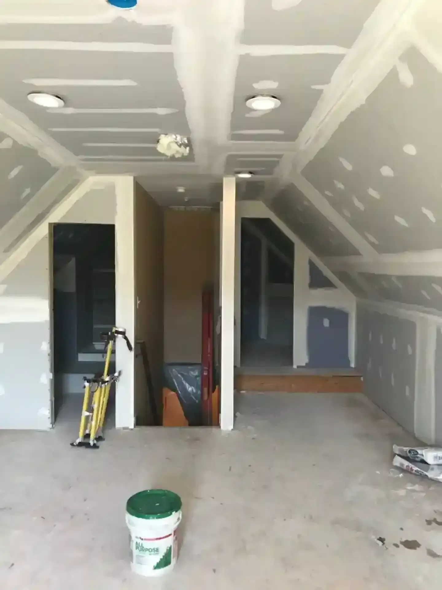 Unfinished attic room with drywall, tools, and a bucket on the floor