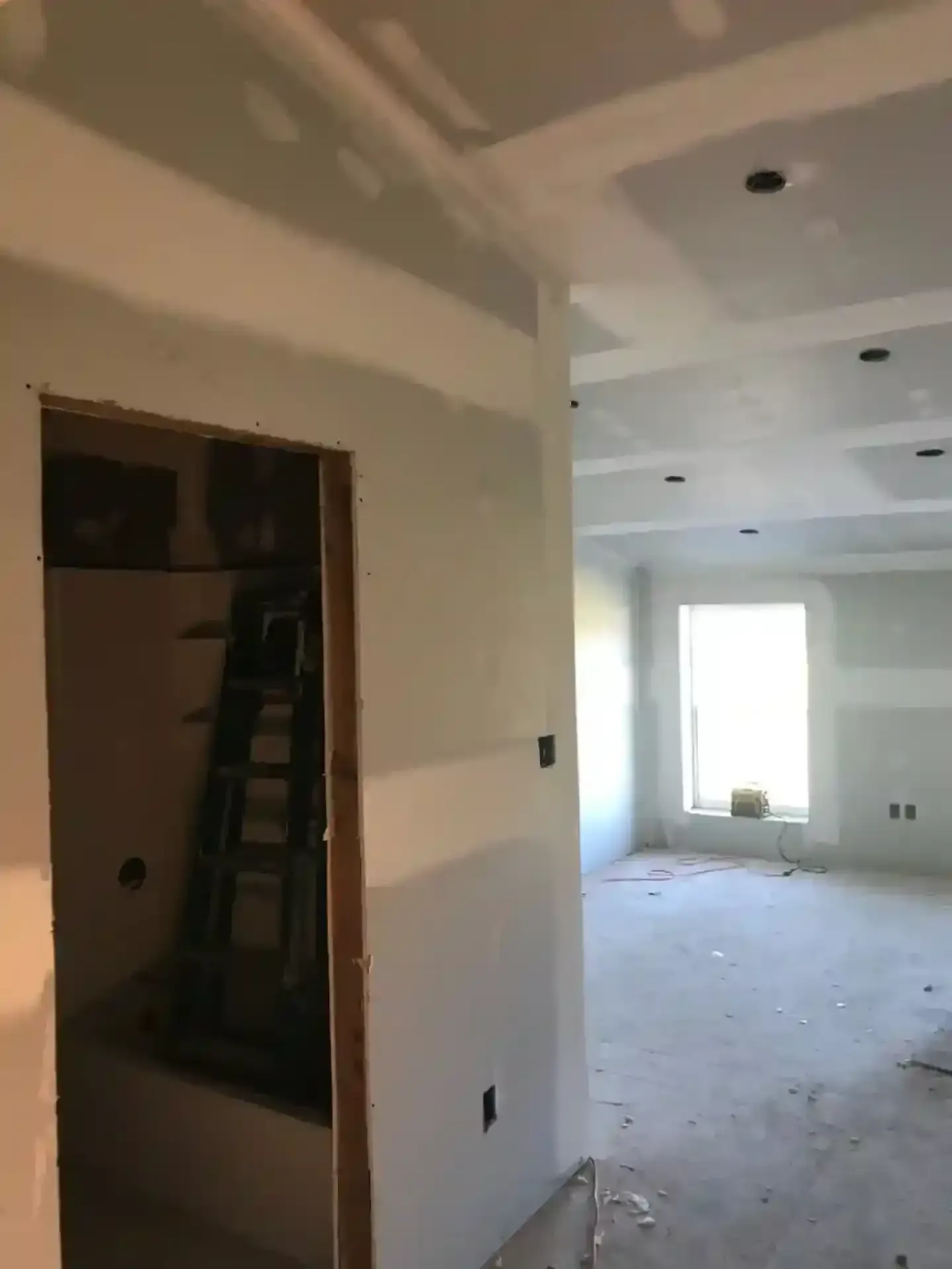 Unfinished hallway and room in a vacant home, with drywall, a ladder, and bright light from a window.
