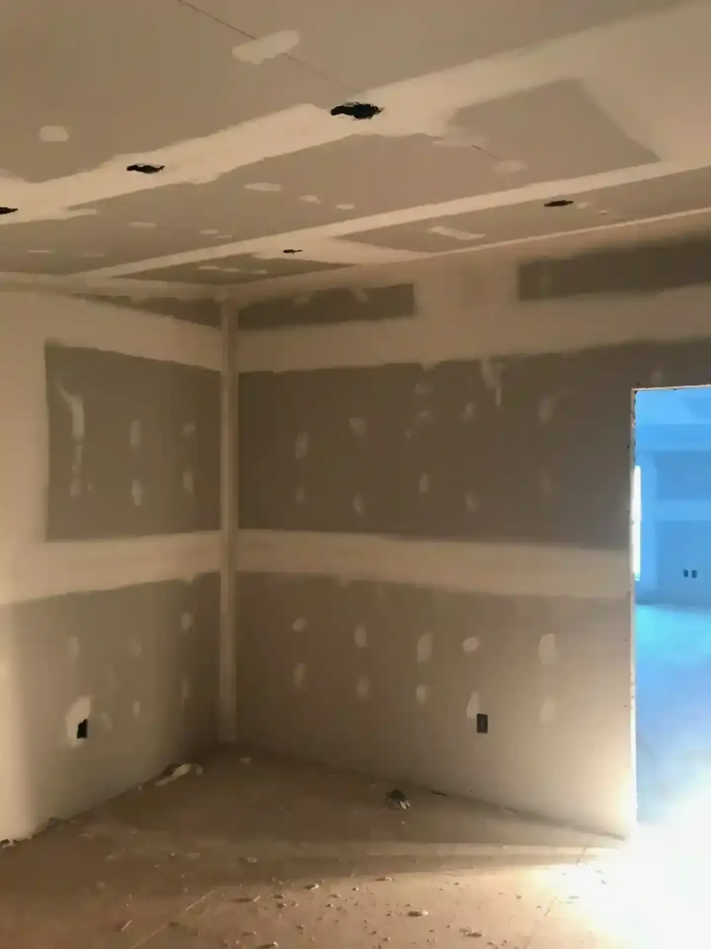 Unfinished drywall room with taped seams and an open doorway letting in blue light