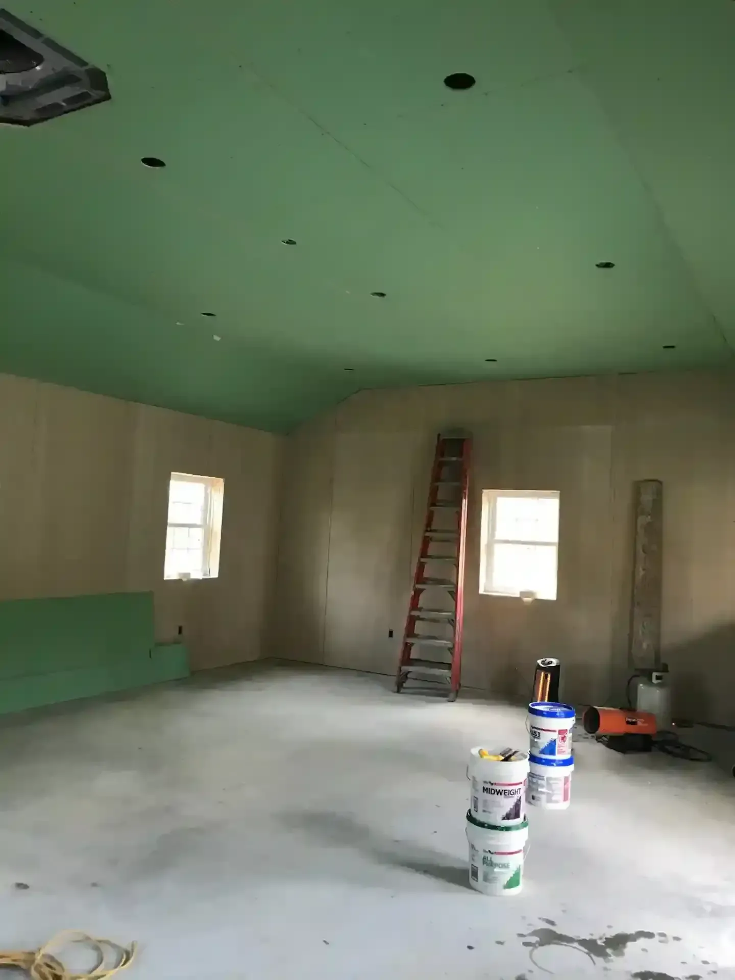 Partially finished room with green ceiling, ladder, buckets, and tools on the floor.