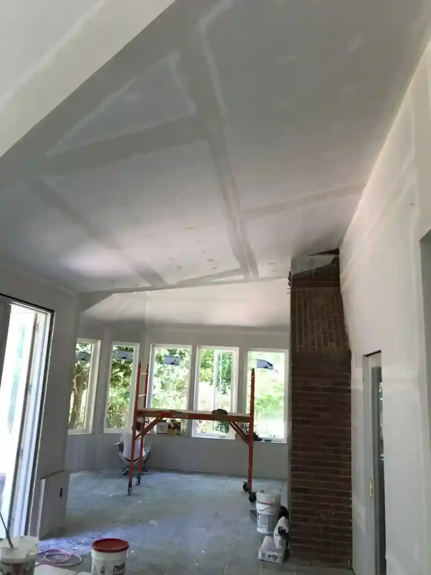Partially finished room with a sloped ceiling, windows, brick column, and construction materials