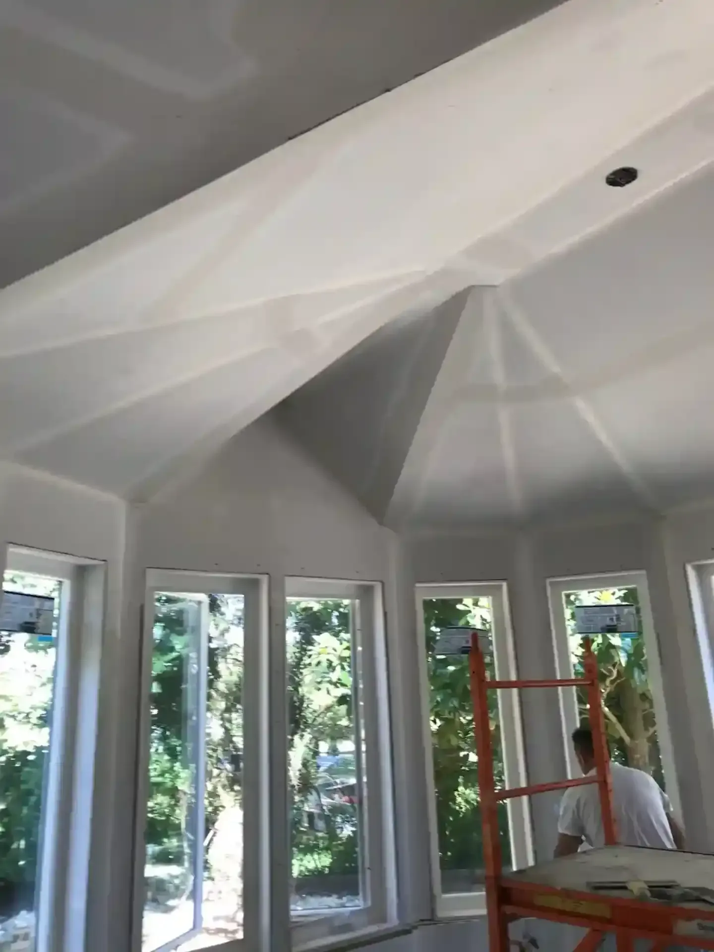 Bright white vaulted room with tall windows; a person on a ladder near the right wall.