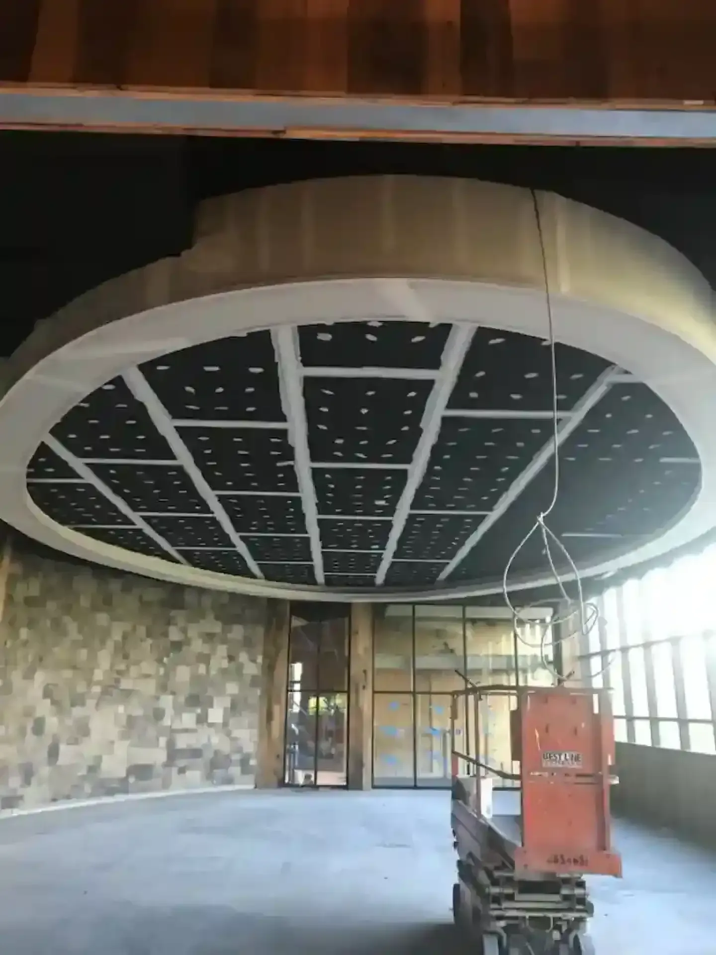 Circular ceiling installation over an open lobby with stone walls and glass doors