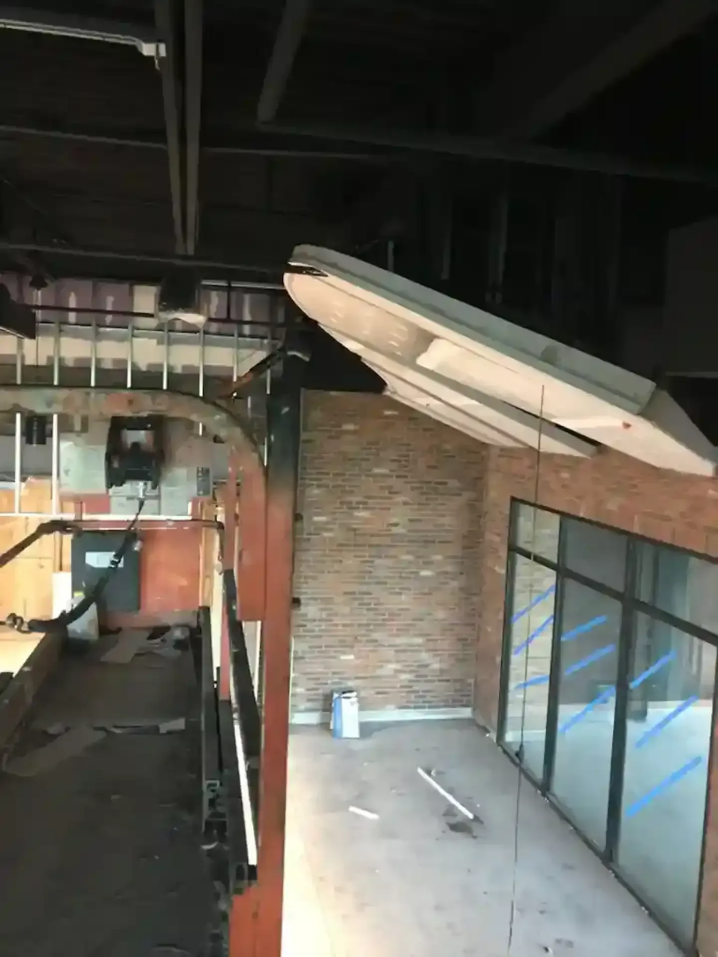 Damaged interior with exposed ceiling, brick wall, and tilted white panel above a hallway.