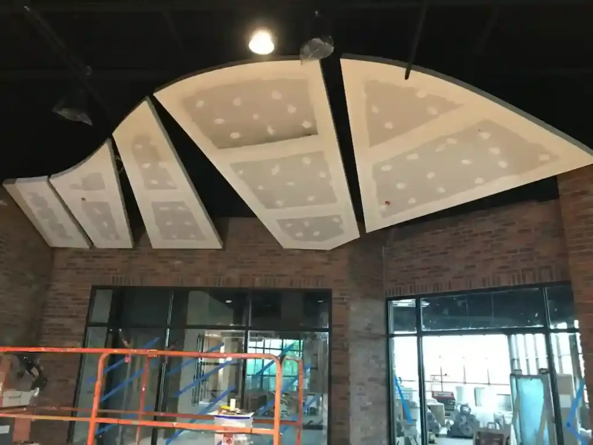 Unfinished ceiling with drywall patches and recessed lights in a brick-walled interior under construction