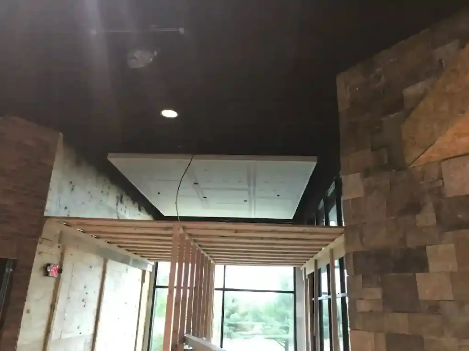 Indoor hallway with dark ceiling, wood slats, stone wall, and bright light at the far end.