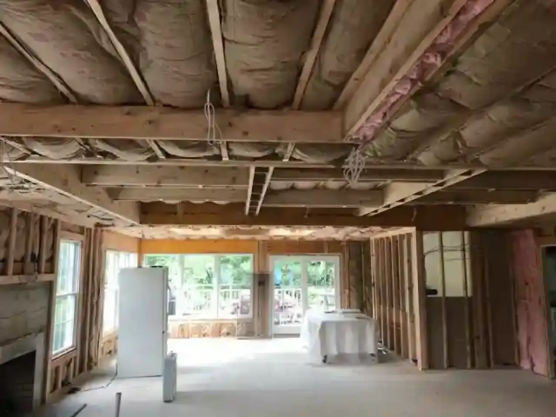 Unfinished room with exposed ceiling joists, windows at the far end, and construction materials inside