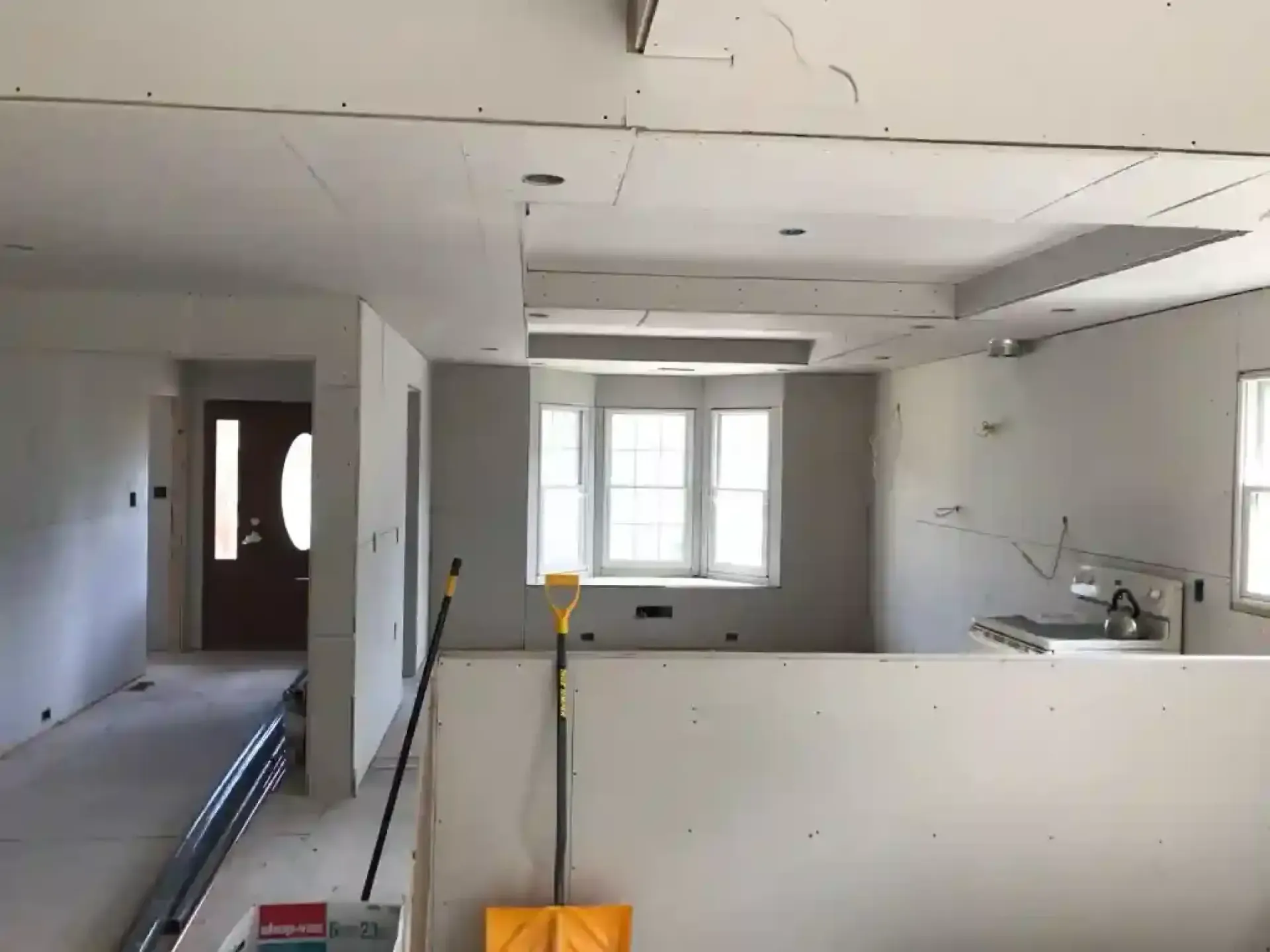 Partially renovated kitchen with white walls, exposed wiring, and windows at the far end