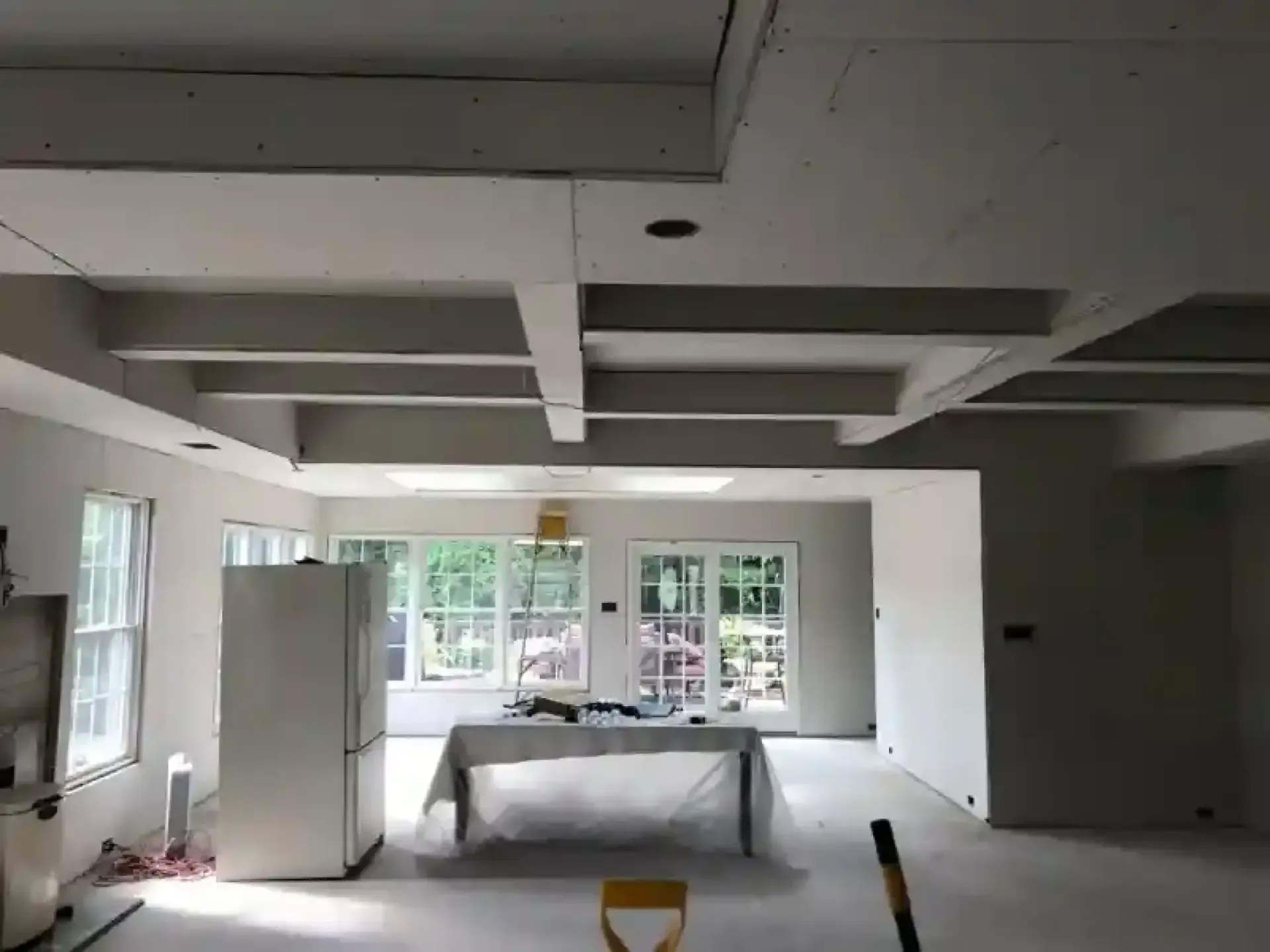 Renovated living room with white walls, exposed ceiling beams, windows, and a couch under construction
