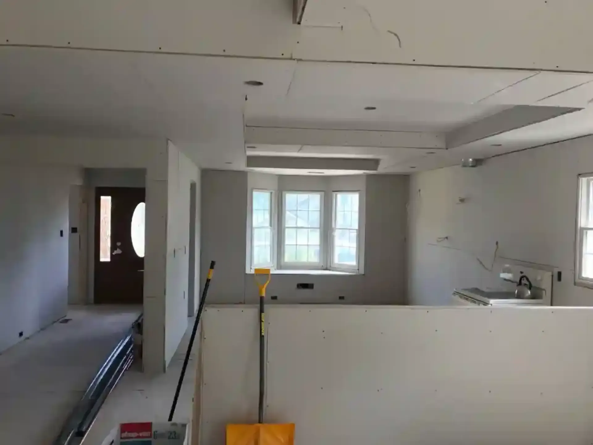 Partially renovated living room with white walls, exposed ceiling, and a window at the far end.