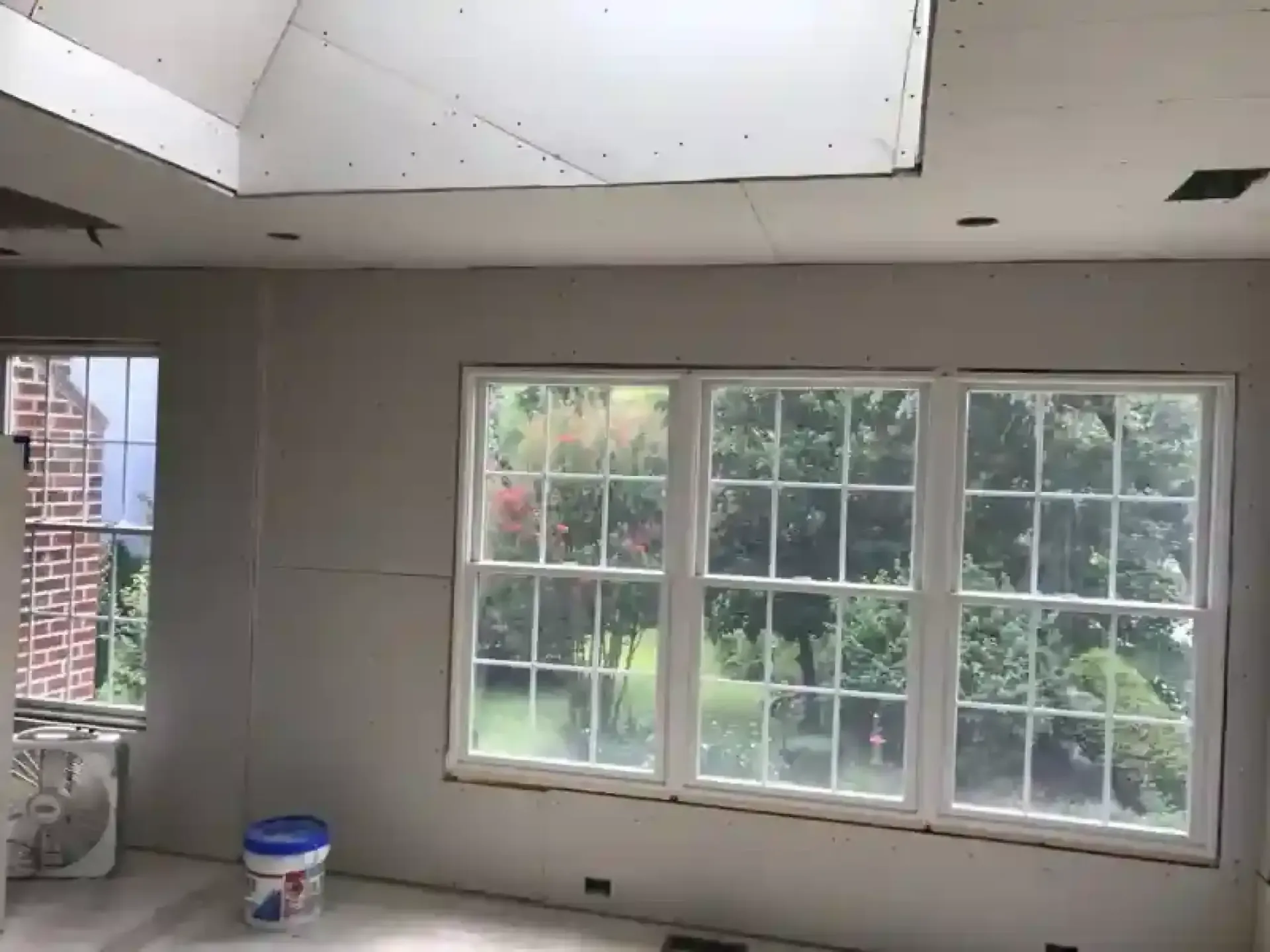 Empty room with white walls, large windows, and a paint bucket on the floor