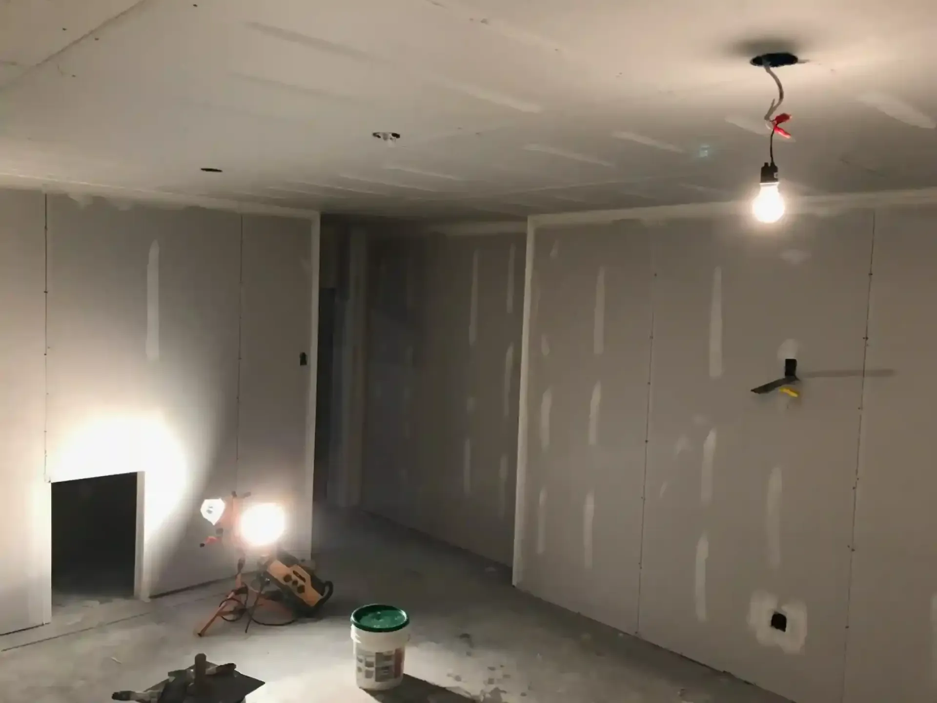 Partially finished room with drywall, exposed light bulb, and construction tools on the floor