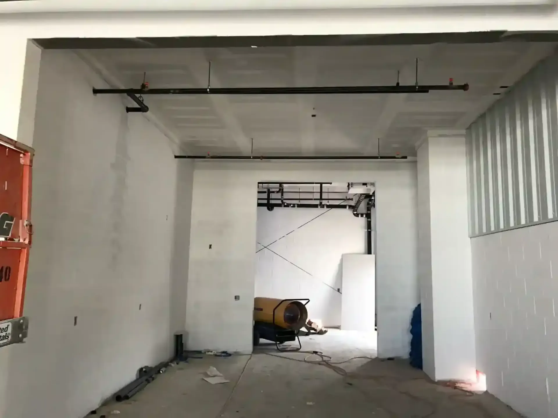 Empty industrial room with white walls, concrete floor, and a yellow machine near an open doorway