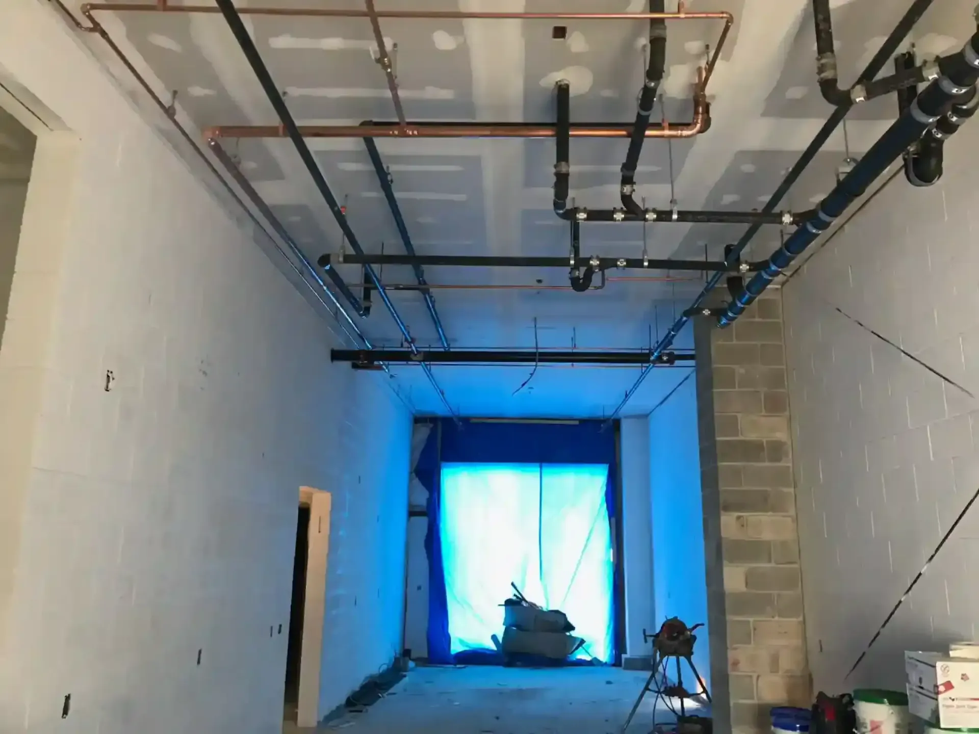 Partially finished room with exposed ceiling pipes, cinderblock wall, and blue-lit window at the end