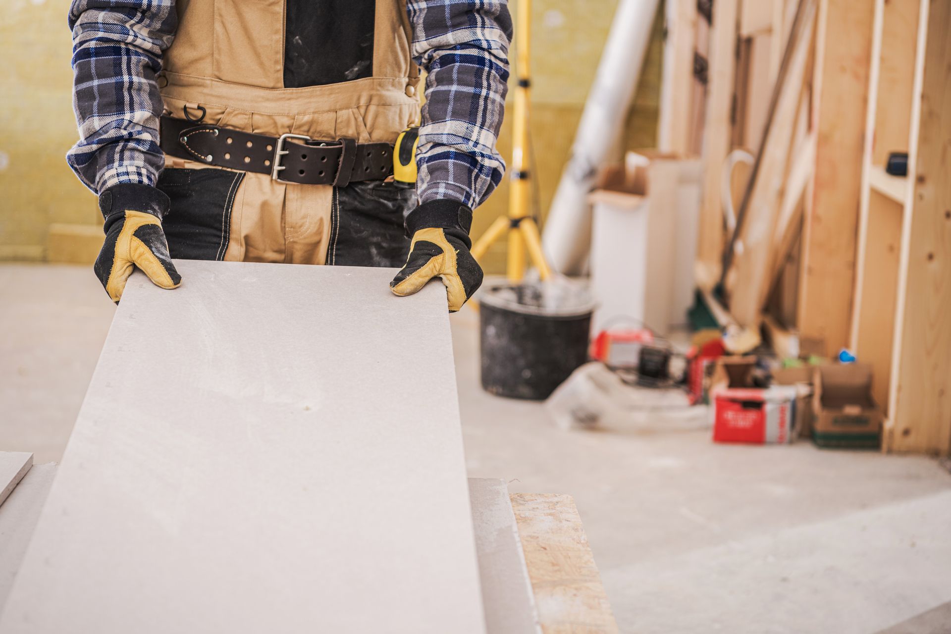 Construction worker holding drywall panel in a renovation site, with lumber and tools in the background