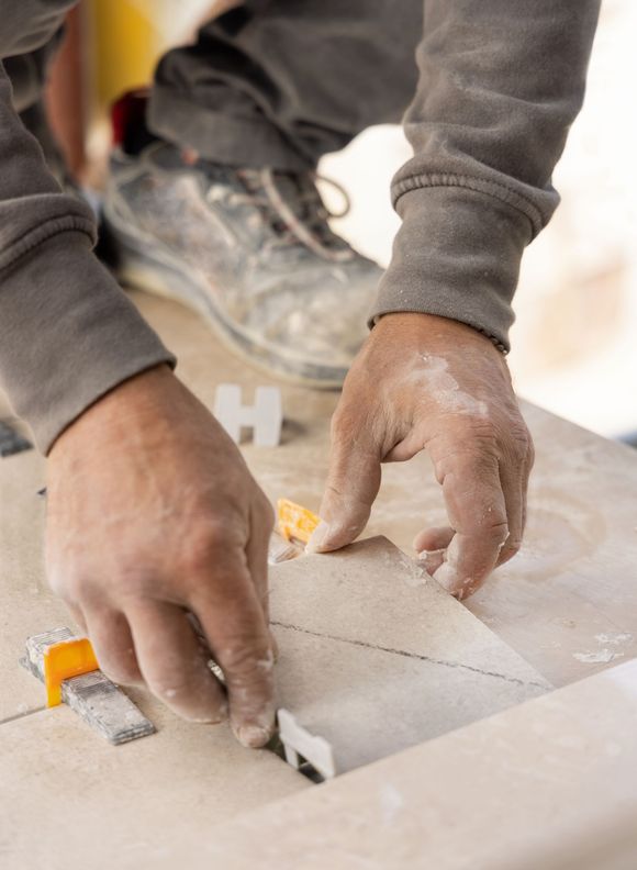 Hands cutting tile with a saw on a dusty work surface