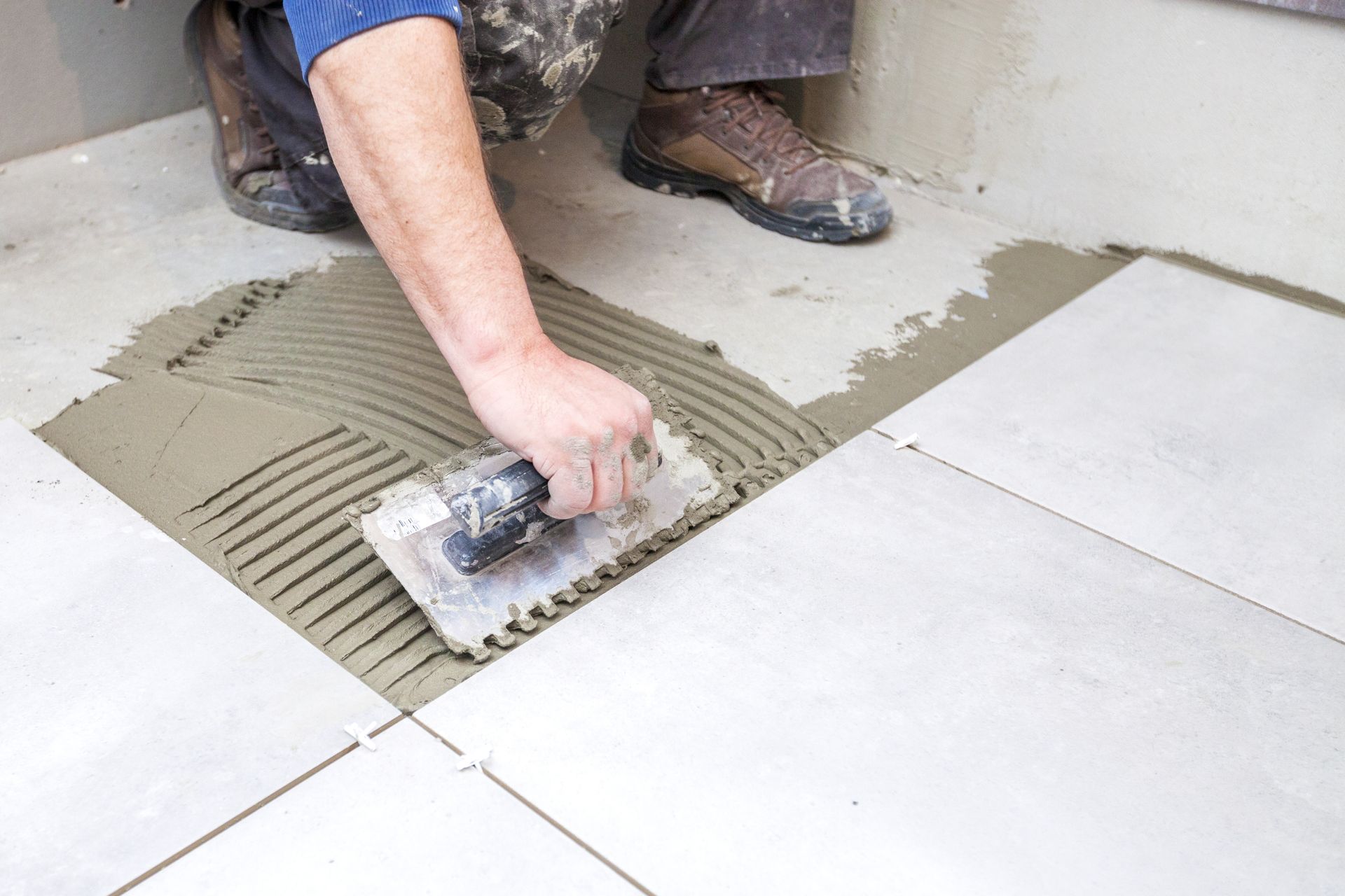 Person spreading tile adhesive on a floor with a trowel beside white tiles
