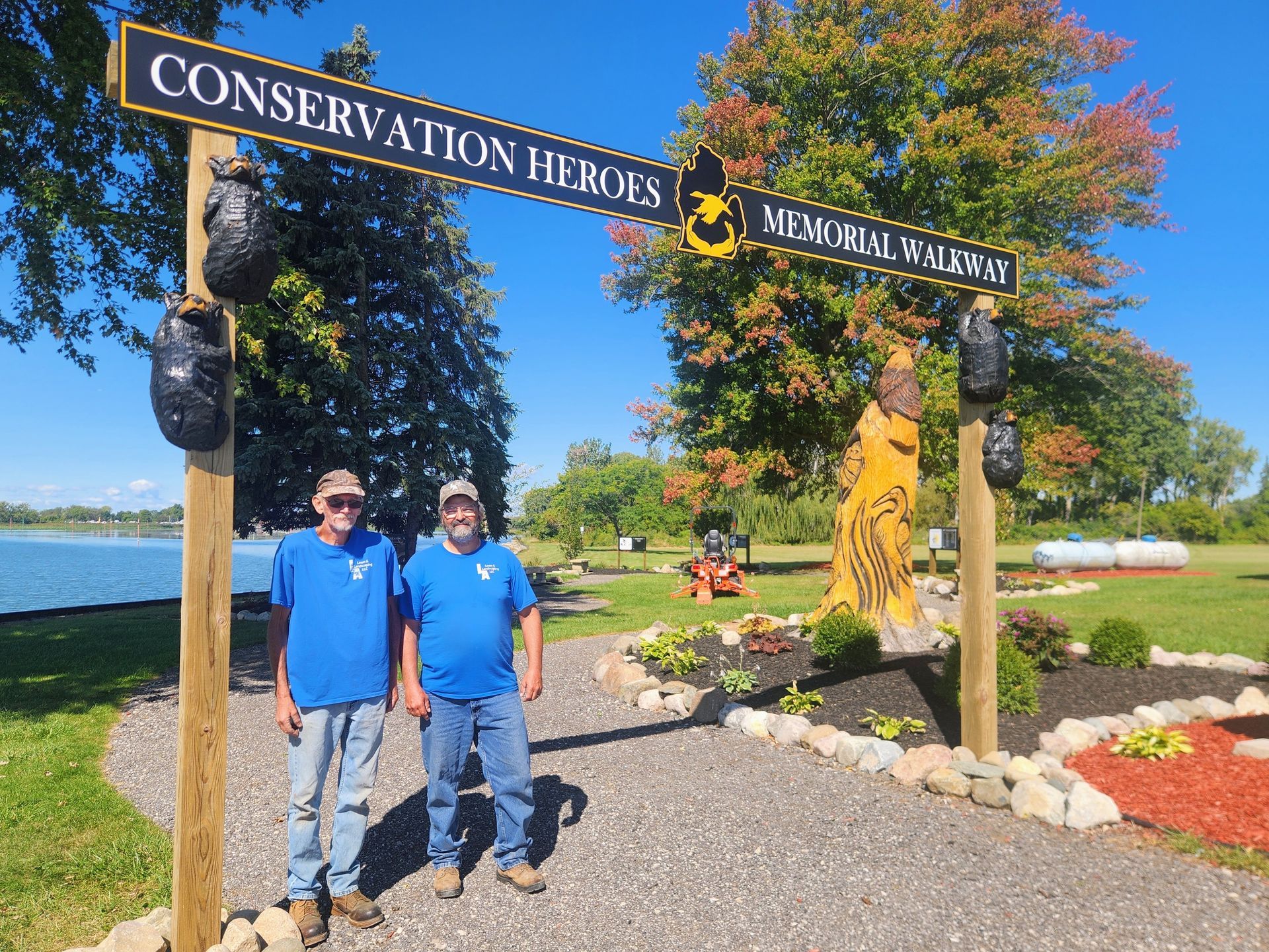 Two people in blue shirts stand beneath a wooden sign that reads