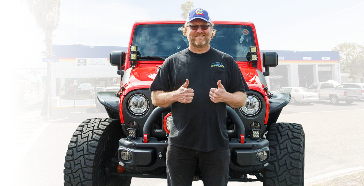 Man standing in front of a red Jeep, giving two thumbs up in a parking lot. | Charlie's Car Care