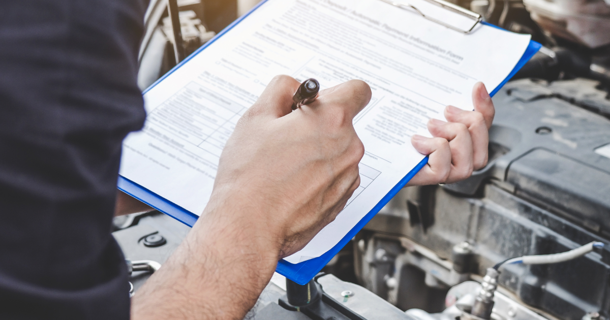 Mechanic writing on a clipboard while inspecting an engine under the hood | Charlie's Car Care