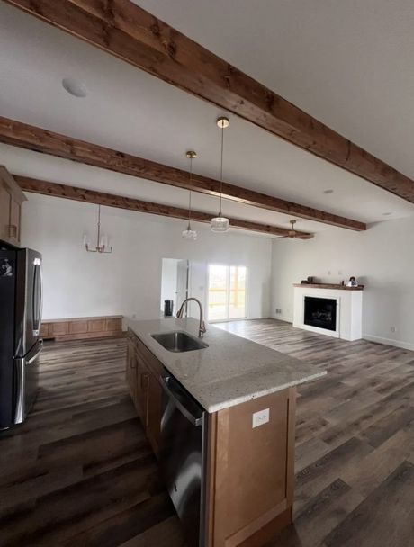 Open-concept kitchen and living area with wood-look flooring, exposed ceiling beams, a central island, and a fireplace.