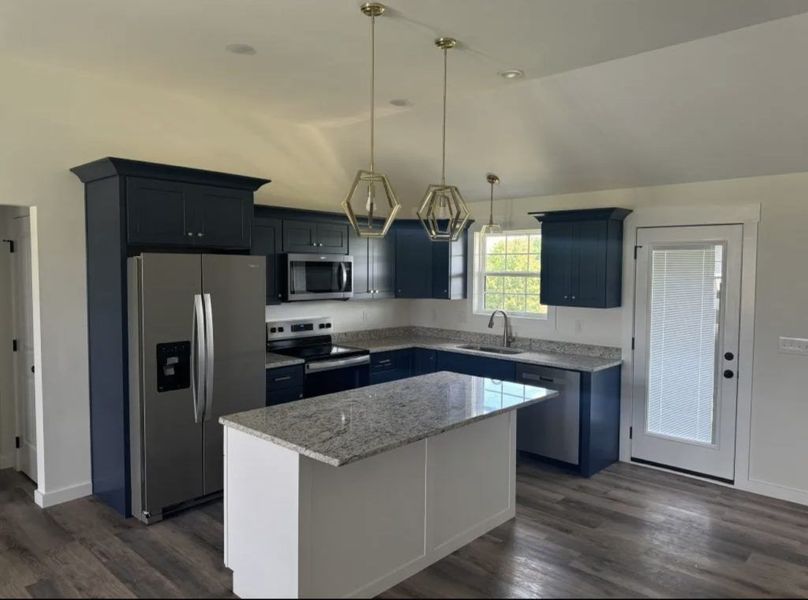 Modern kitchen with dark blue cabinets, granite countertops, a white kitchen island, and stainless steel appliances.